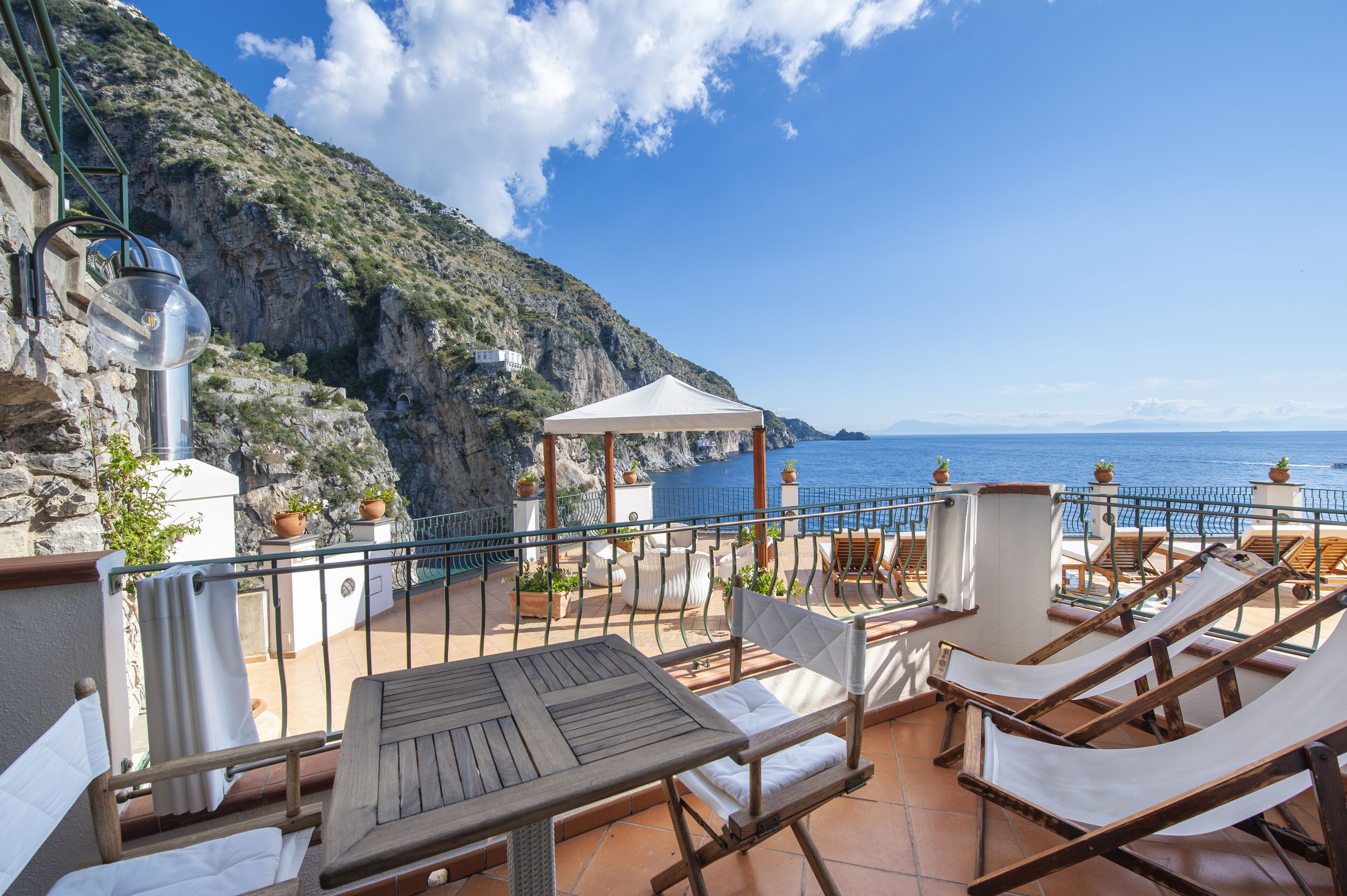A terrace with a table and chairs, a white canopy, and a view of the sea.