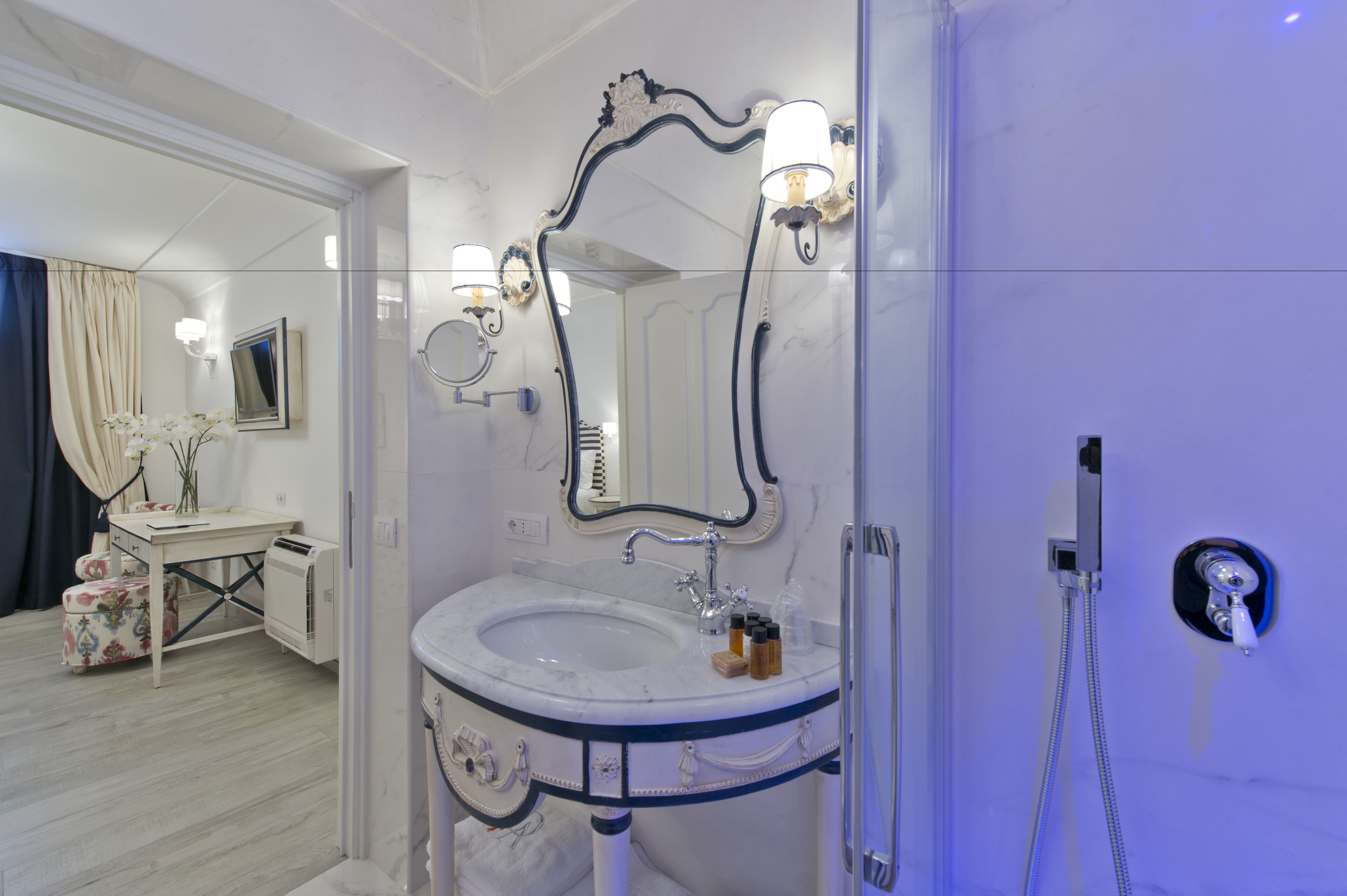Une salle de bain avec un lavabo blanc, un miroir agrémenté de lumières décoratives et une douche.