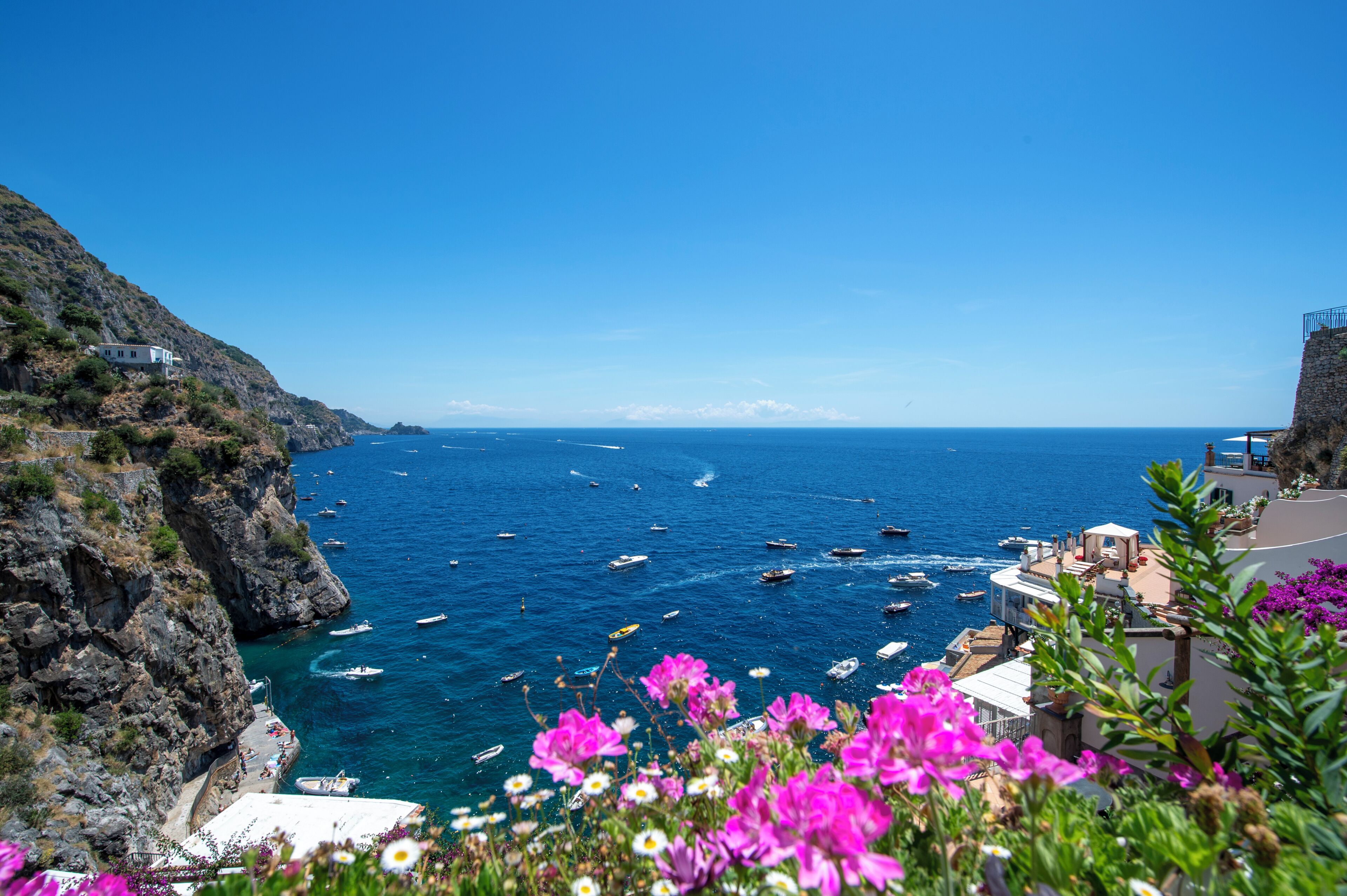 A coastal view with boats, rocky cliffs, and buildings.