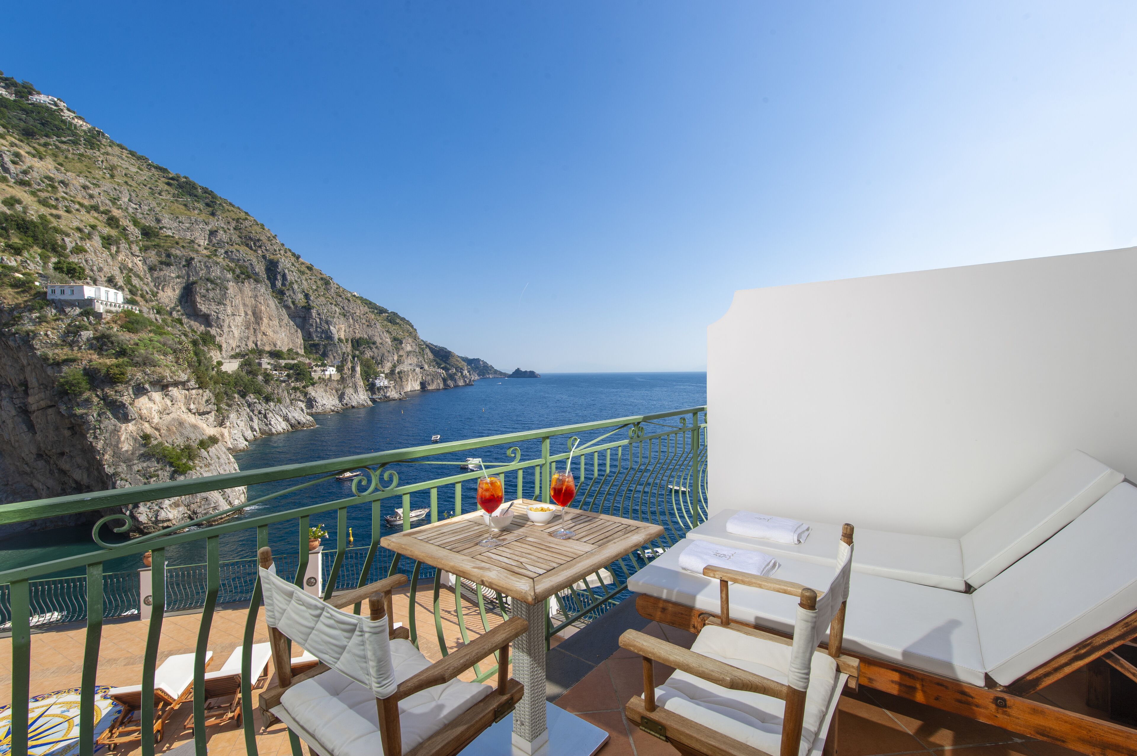 A balcony with a table and chairs overlooking a coastal cliff and sea.