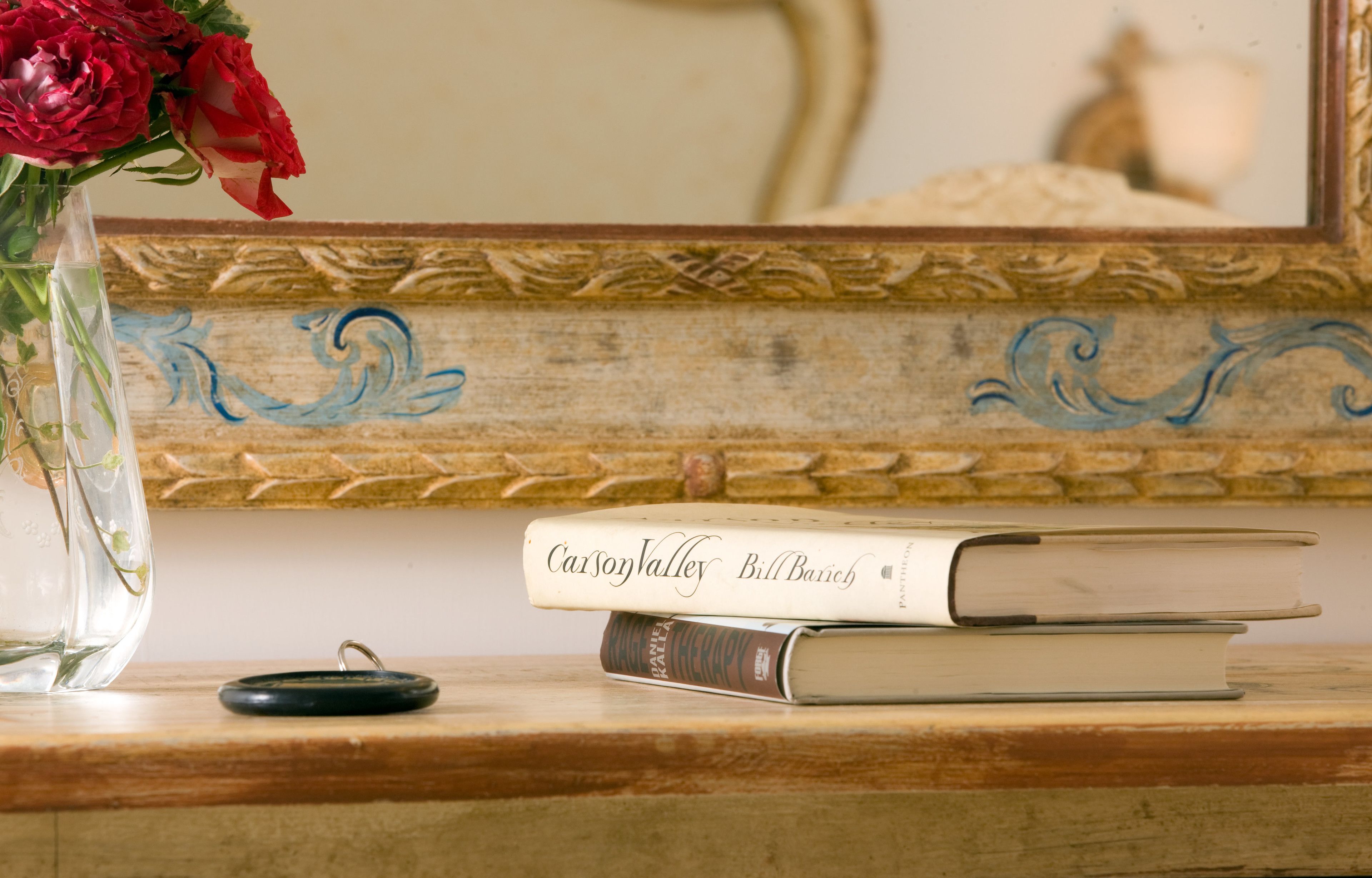 Une table en bois sur laquelle se trouve un vase de fleurs rouges, une pile de livres et un petit objet noir.