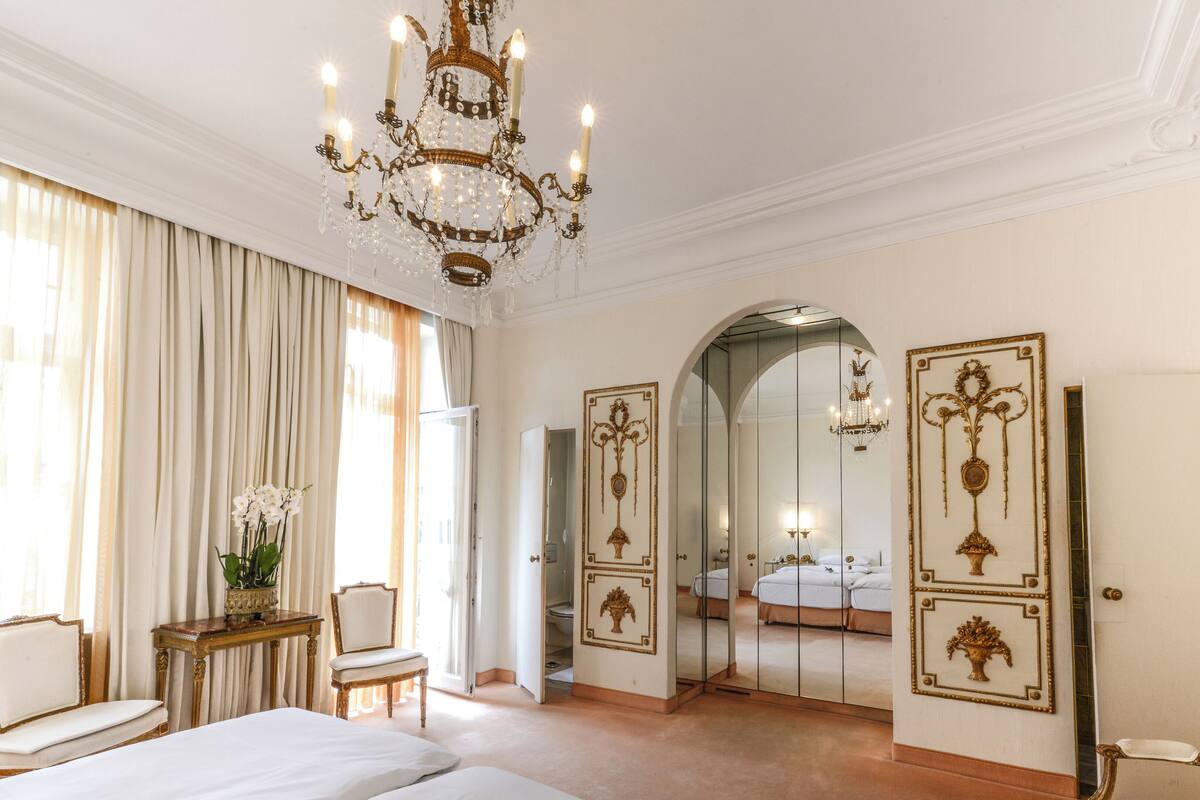 A luxurious bedroom with a large bed, a chandelier, and ornate wall decorations.