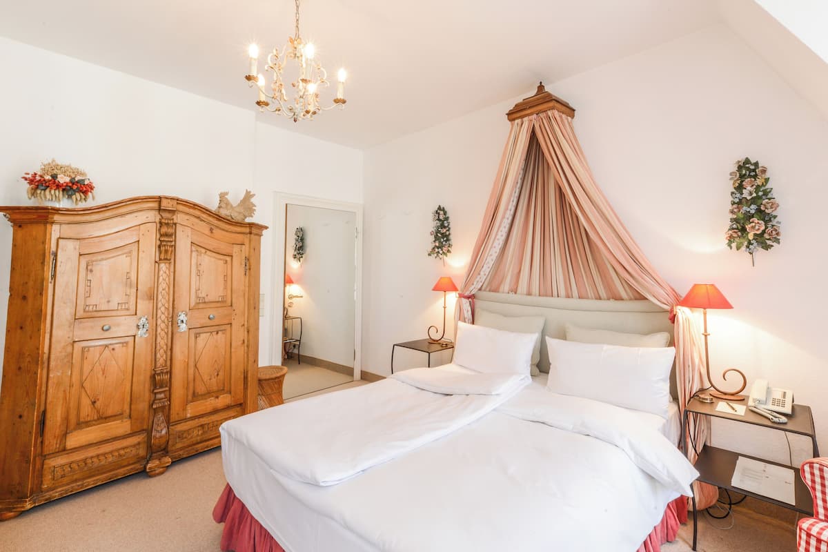 A bedroom with a four-poster bed, wooden wardrobe, and a chandelier.