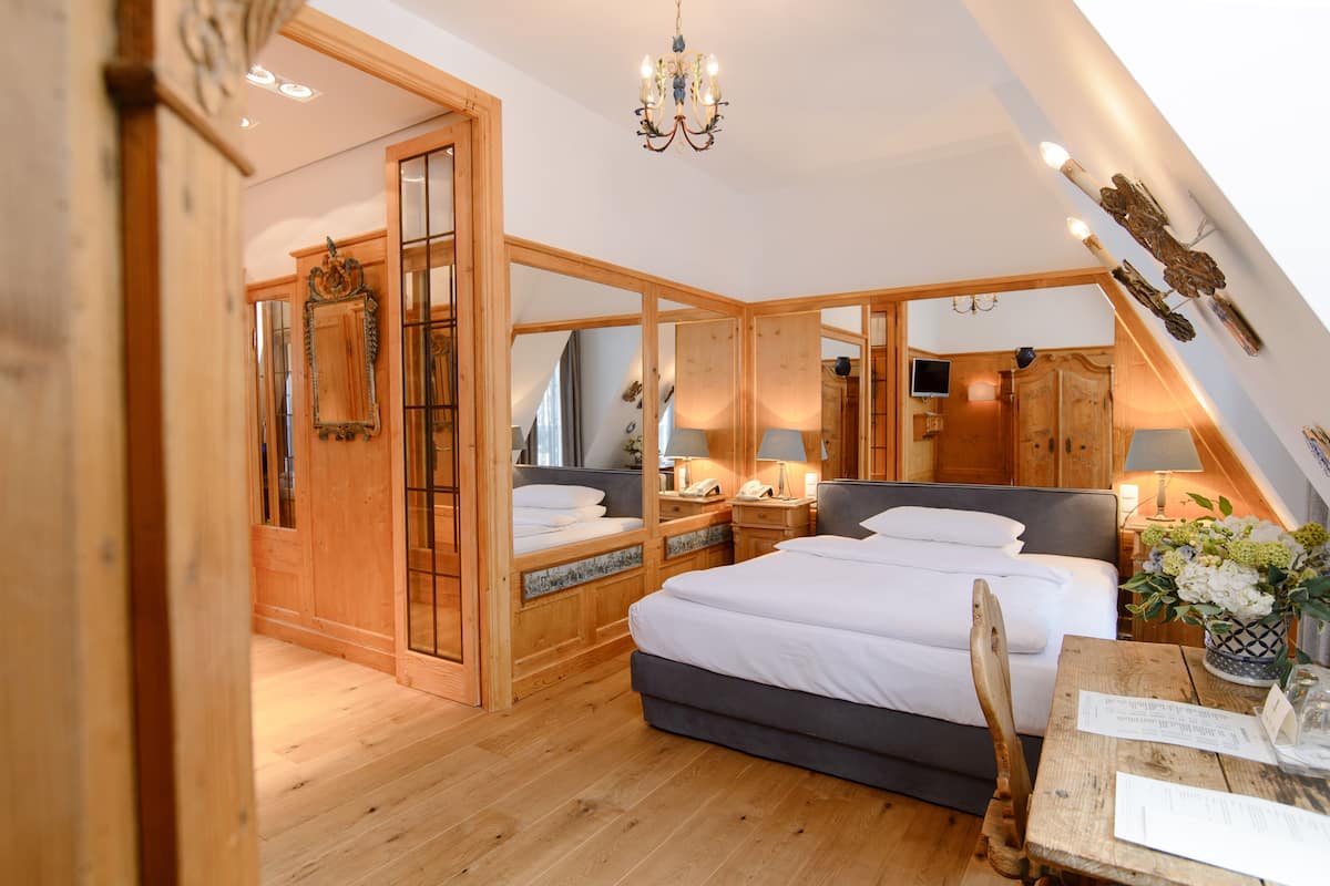 A bedroom with a large bed, wooden walls, a chandelier, and a wooden table with a vase of flowers.