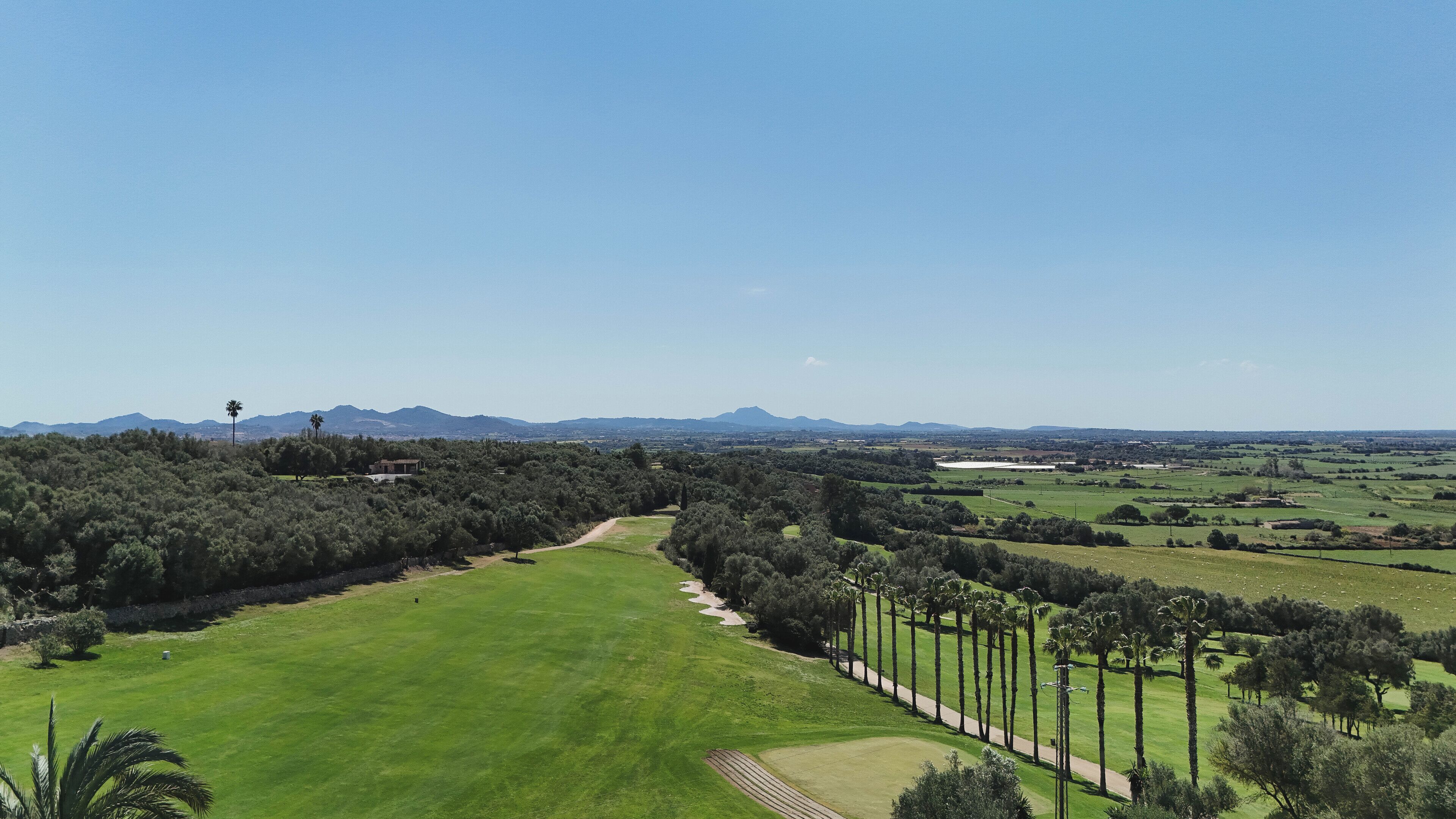 Un campo de golf con un sendero despejado, rodeado de árboles y una cordillera distante.