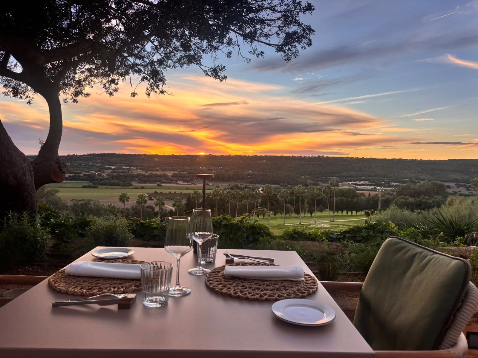 A table set for two with a view of a sunset over a landscape.