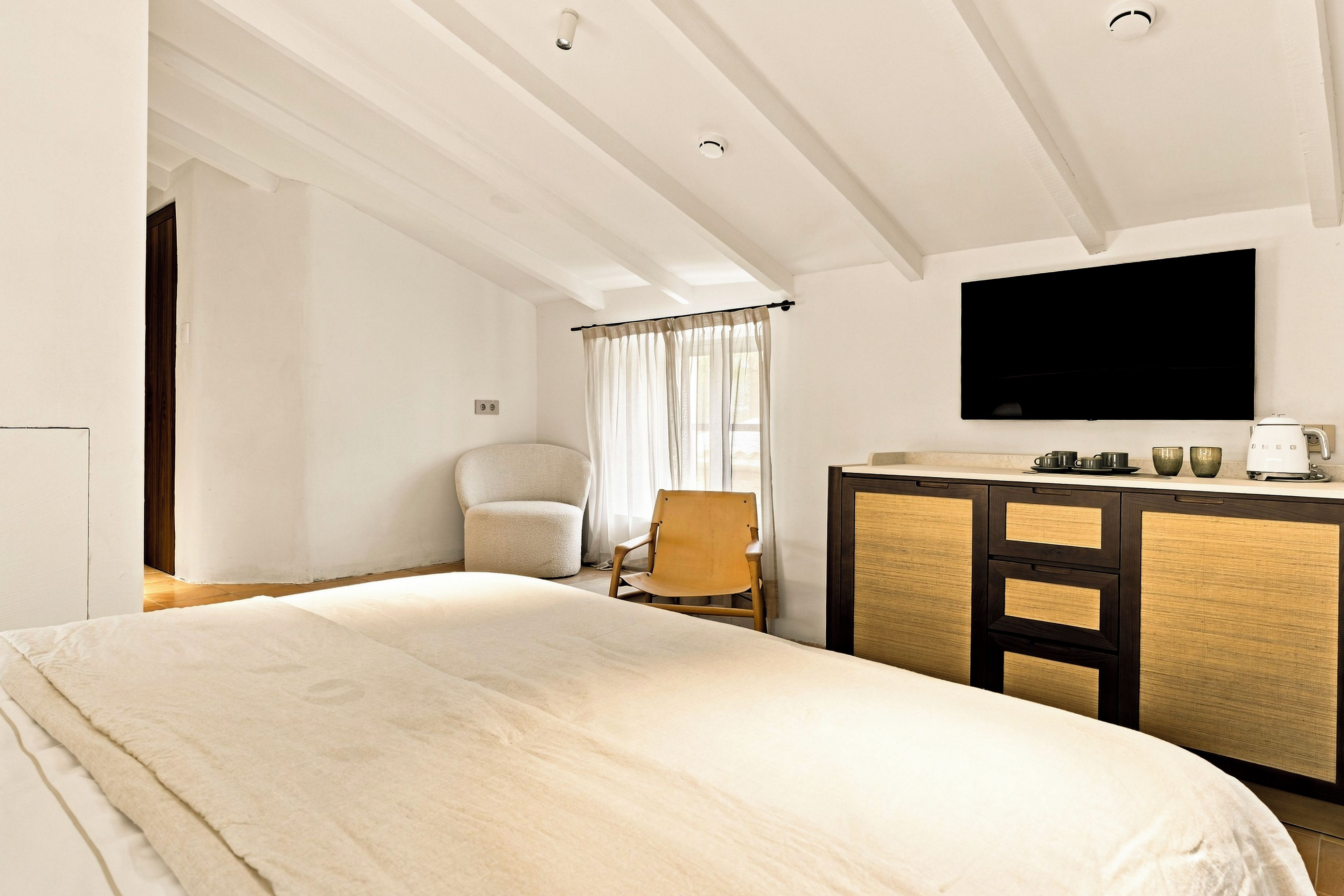 Quarto de hotel com cama grande, escrivaninha, televisão de tela plana, cadeira e janela com cortinas.