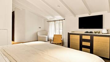 Quarto de hotel com cama grande, escrivaninha, televisão de tela plana, cadeira e janela com cortinas.