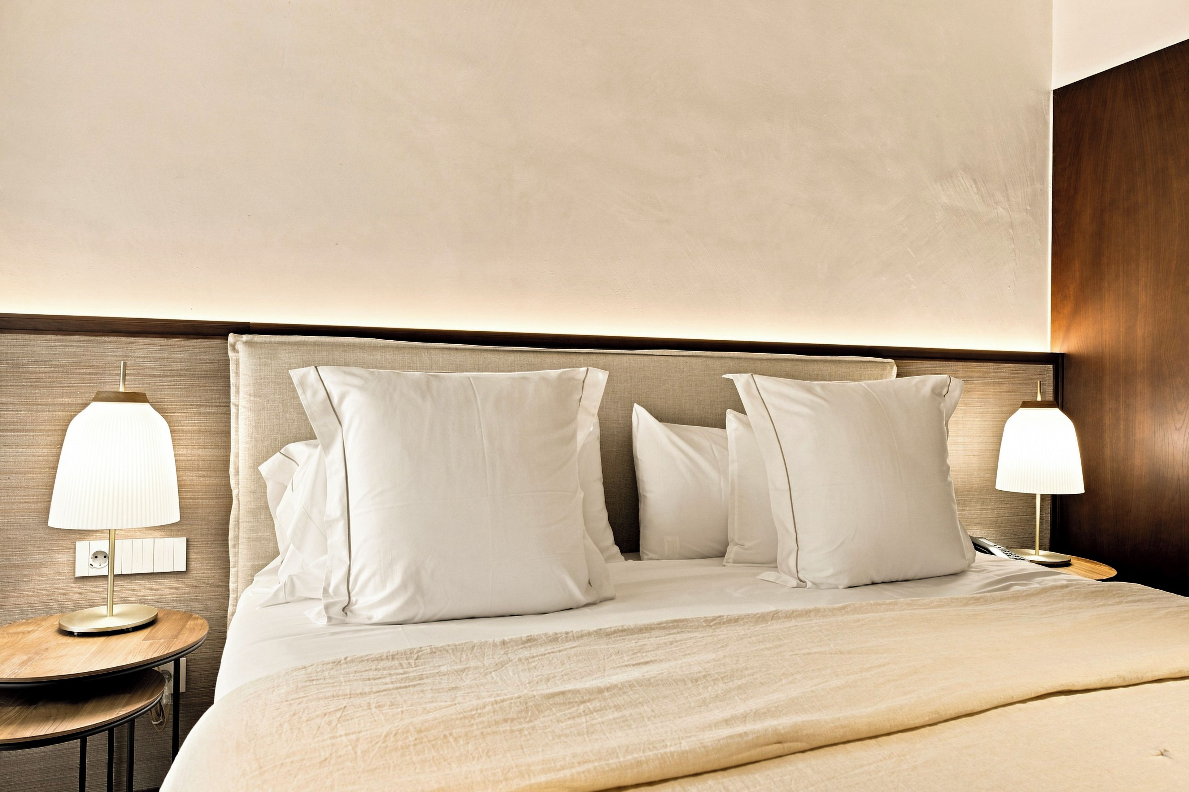 Een hotelkamer met een net opgemaakt bed, twee nachtkastjes met lampen en een houten hoofdeinde.