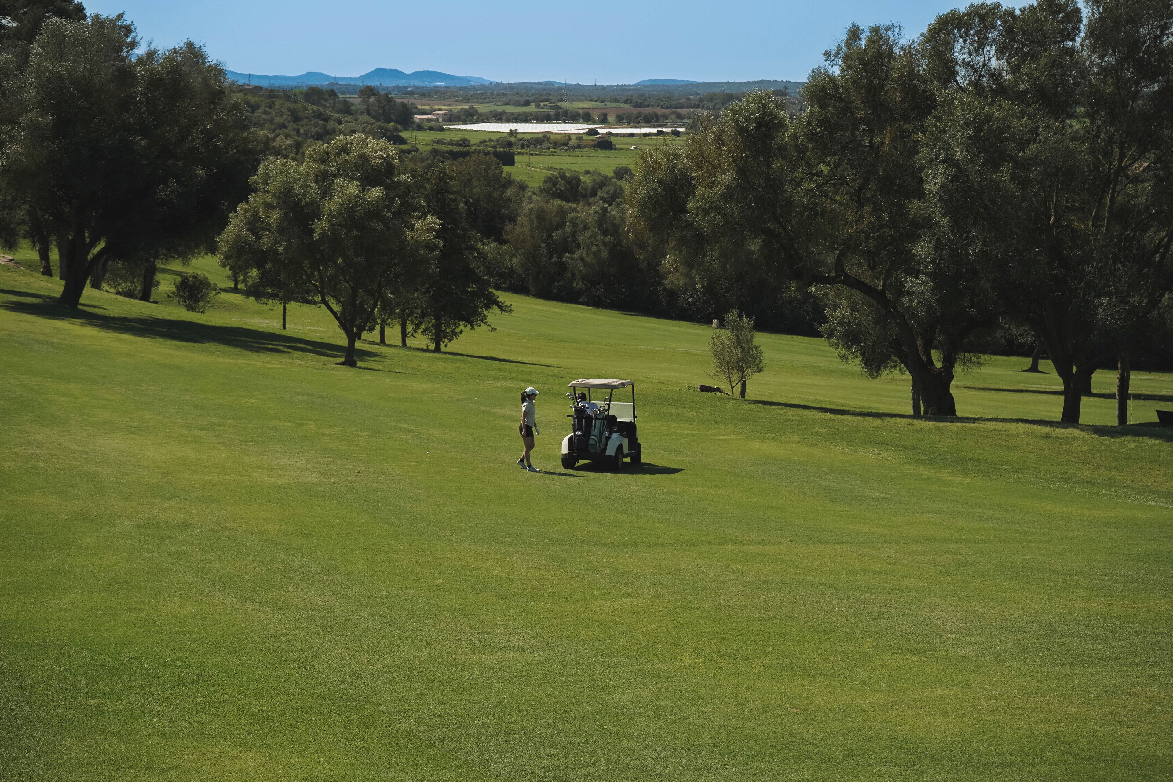 Campo de golf con un carrito y una persona de pie en el green.