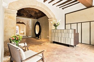 Un área de recepción con un arco de piedra, un espejo grande, una zona de estar con una silla y un piso con baldosas.