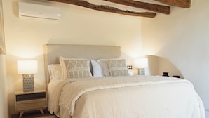 Quarto com cama, mesas de cabeceira, abajur e ar condicionado fixado na parede.