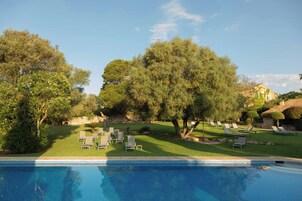 Zona de piscina con sillas de descanso y un edificio de piedra al fondo.