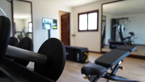 A gym with exercise equipment, a bench, and a mirror reflecting the room. - Rotana la Reserva (Manacor)