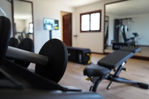 A gym with exercise equipment, a bench, and a mirror reflecting the room. - Rotana la Reserva (Manacor)