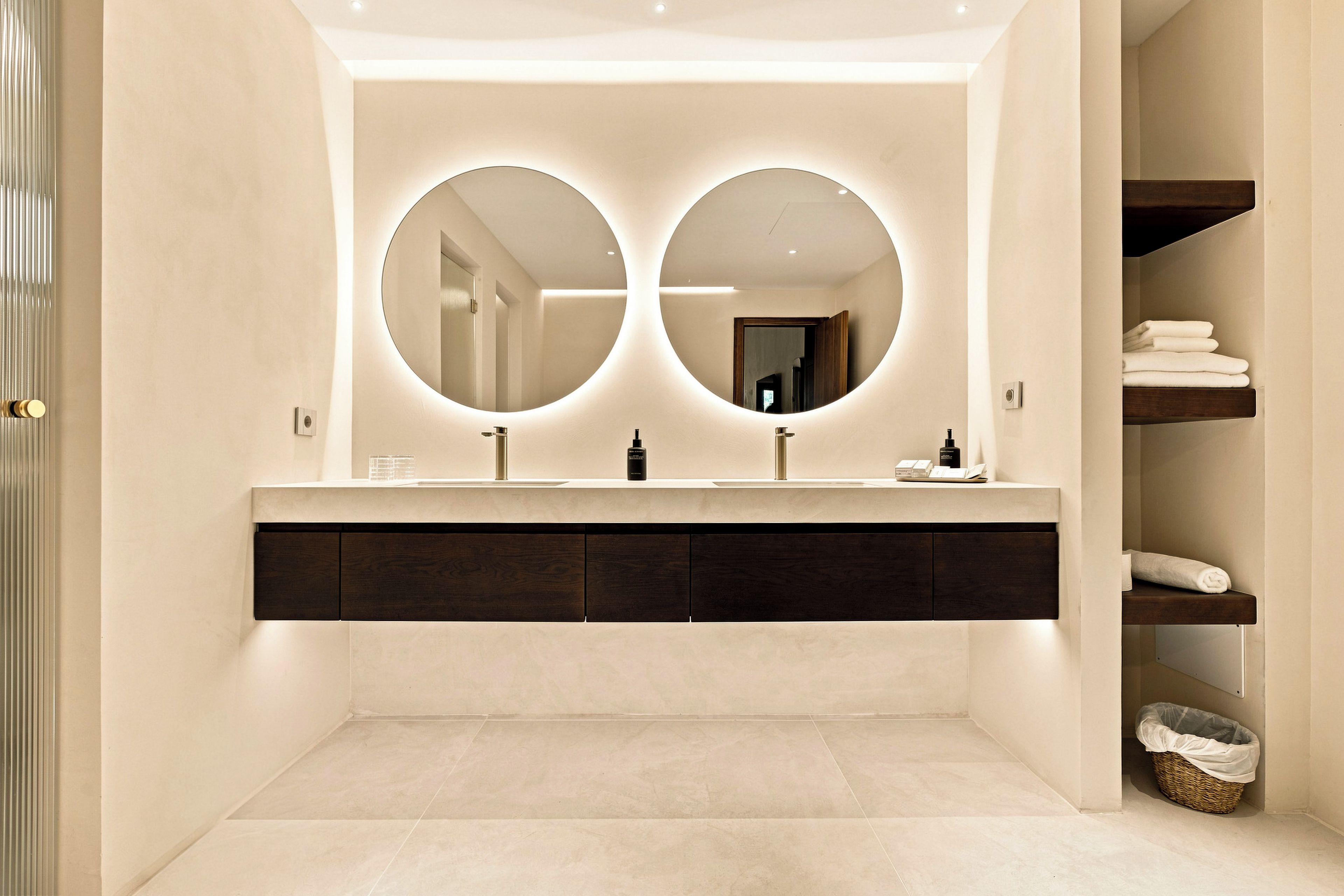 A modern bathroom with a double vanity, two round mirrors, and a built-in shelf with towels.