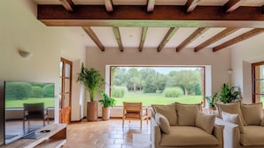 A spacious living room with a large window, a television, a sofa, and a coffee table. - Rotana la Reserva (Manacor)