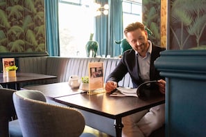 A man seated at a table in a restaurant with a menu, a small plant, and a decorative vase. - Queens Hotel & Spa Bournemouth (Bournemouth)