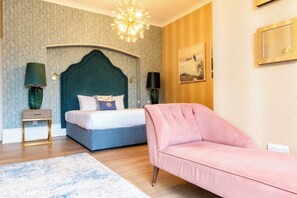 A bedroom with a bed, a pink sofa, a chandelier, and a painting on the wall. - Queens Hotel & Spa Bournemouth (Bournemouth)