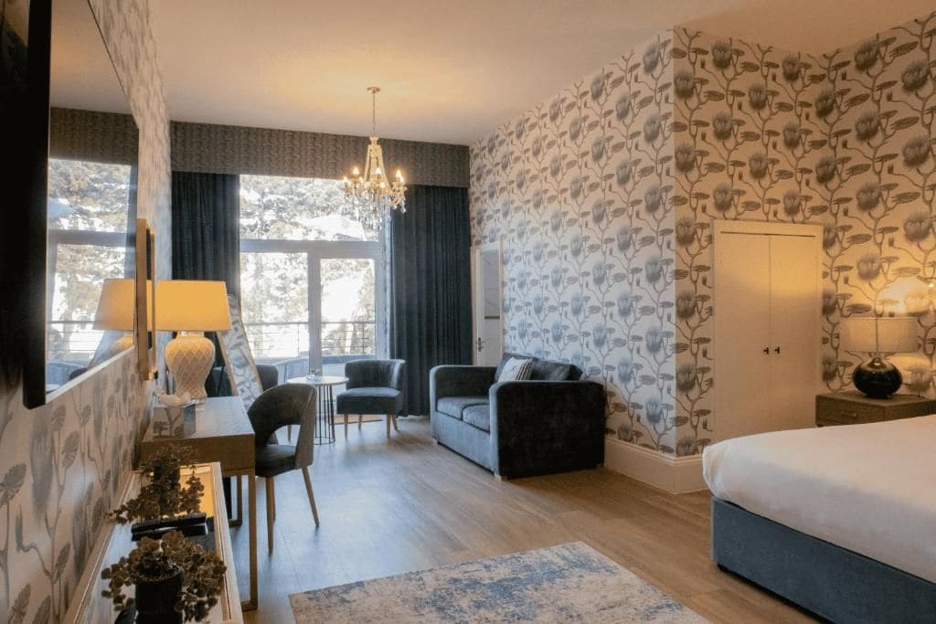 Een hotelkamer met een bed, een bureau met een lamp, een sofa, een kroonluchter en uitzicht op bomen.