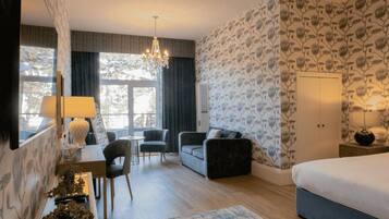 Een hotelkamer met een bed, een bureau met een lamp, een sofa, een kroonluchter en uitzicht op bomen.