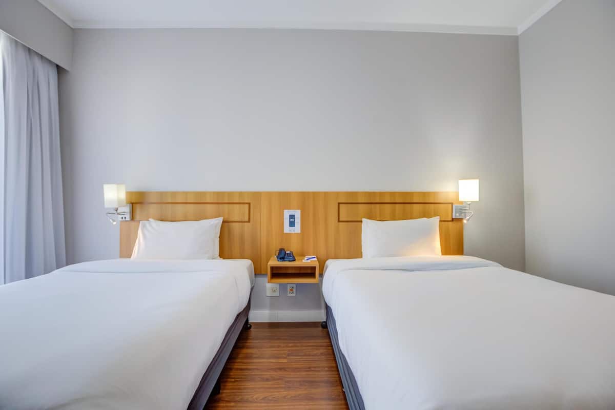 Ein Hotelzimmer mit zwei Betten, einem hölzernen Kopfteil, Nachttischlampen, einem Nachttisch und einem Telefon.