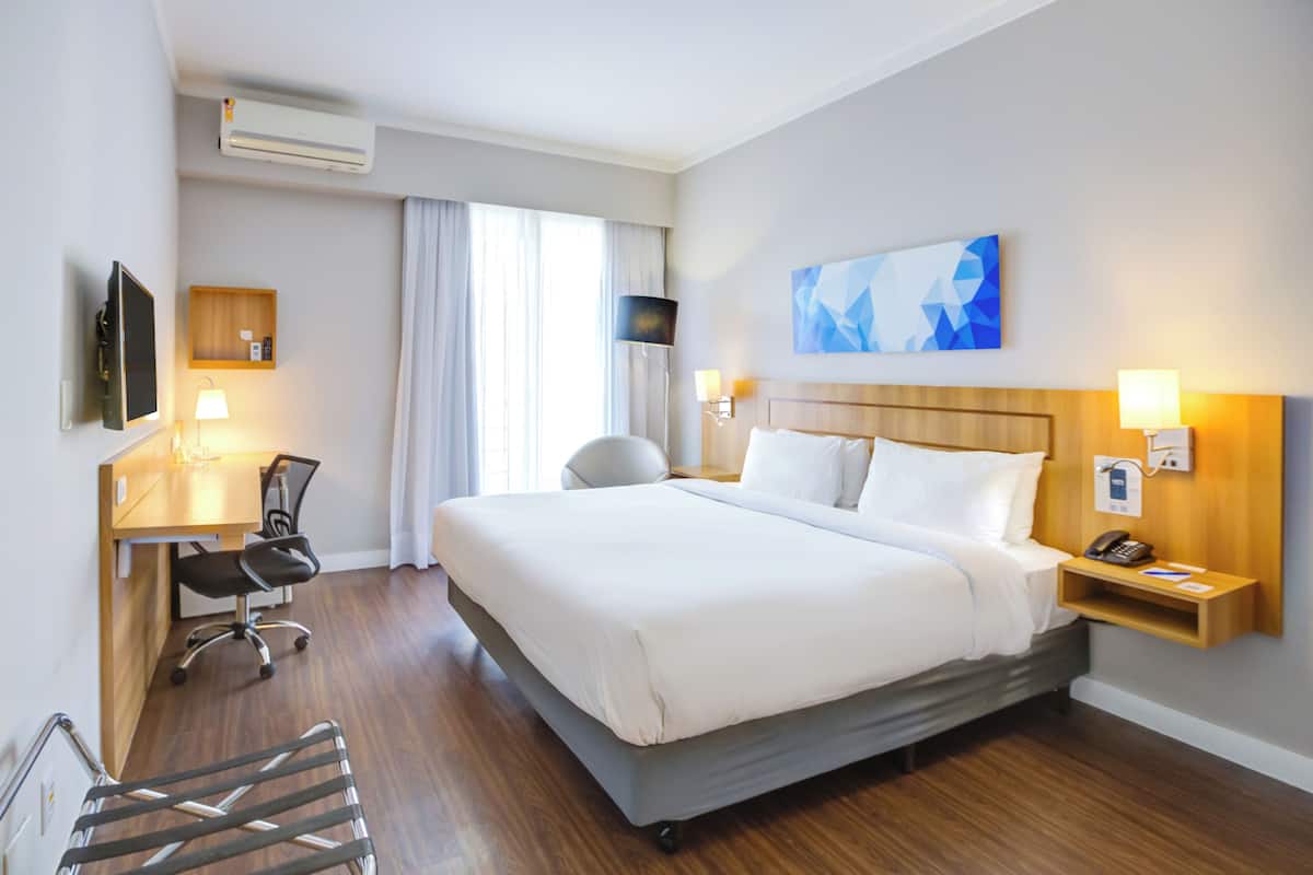 Ein Hotelzimmer mit Bett, Schreibtisch, Stuhl und einem an der Wand befestigten Fernseher.