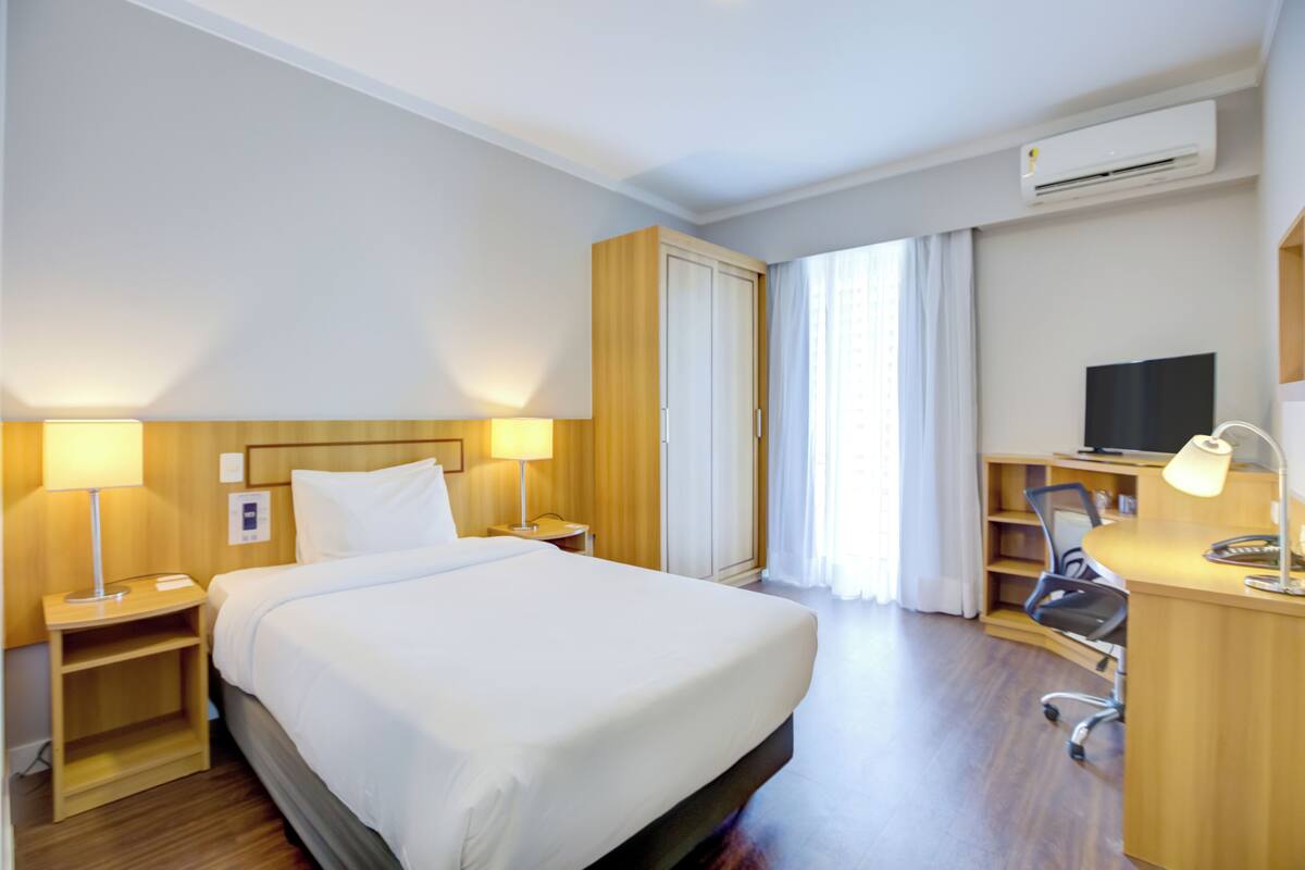 Ein Hotelzimmer mit einem Bett, einem Schreibtisch mit Stuhl, einem Fernseher und einer Klimaanlage.