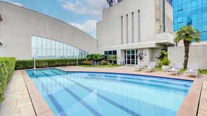 A swimming pool with lounge chairs, a modern building with large windows, and a clear sky. - Comfort Hotel Ibirapuera (São Paulo)