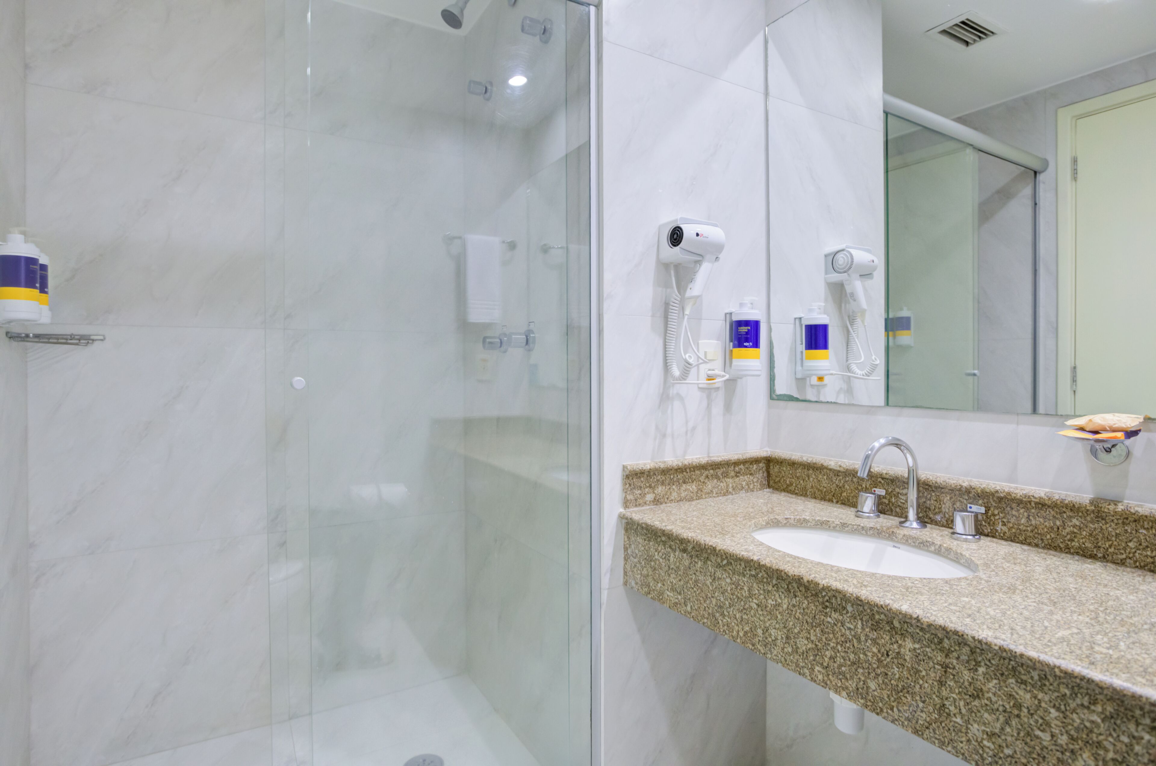 Een moderne badkamer met een douche in een glazen cabine, een wastafel met granieten blad en een spiegel.
