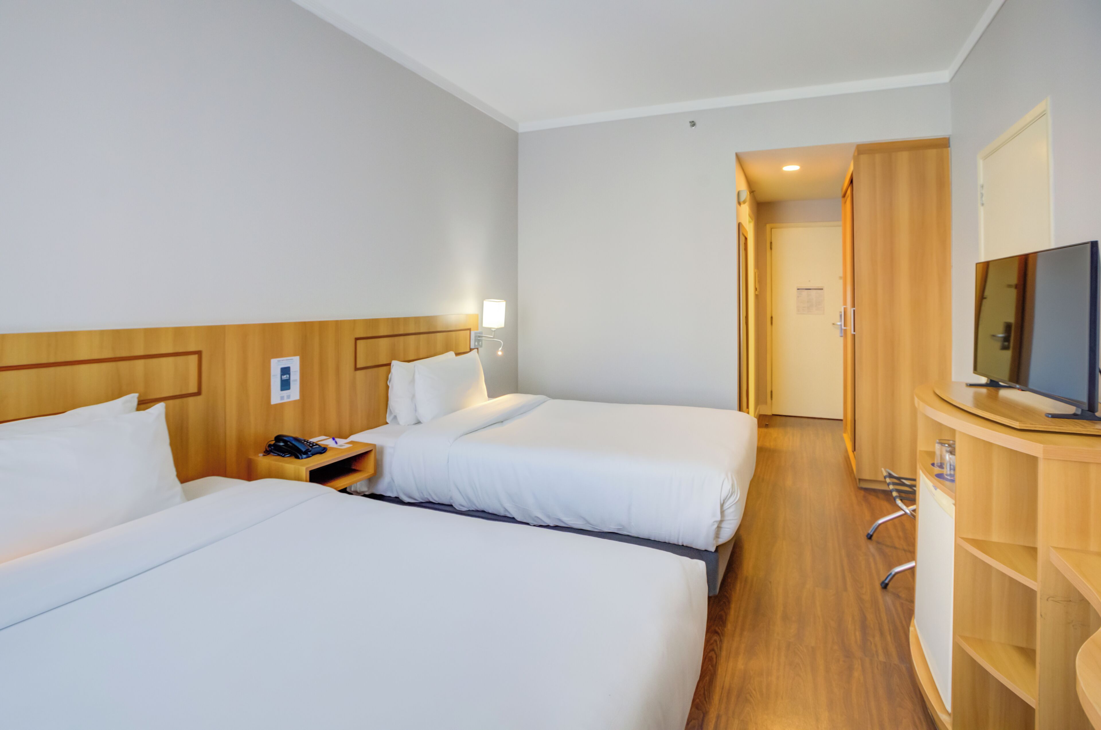 A hotel room with two beds, a TV, a desk, and a wardrobe.