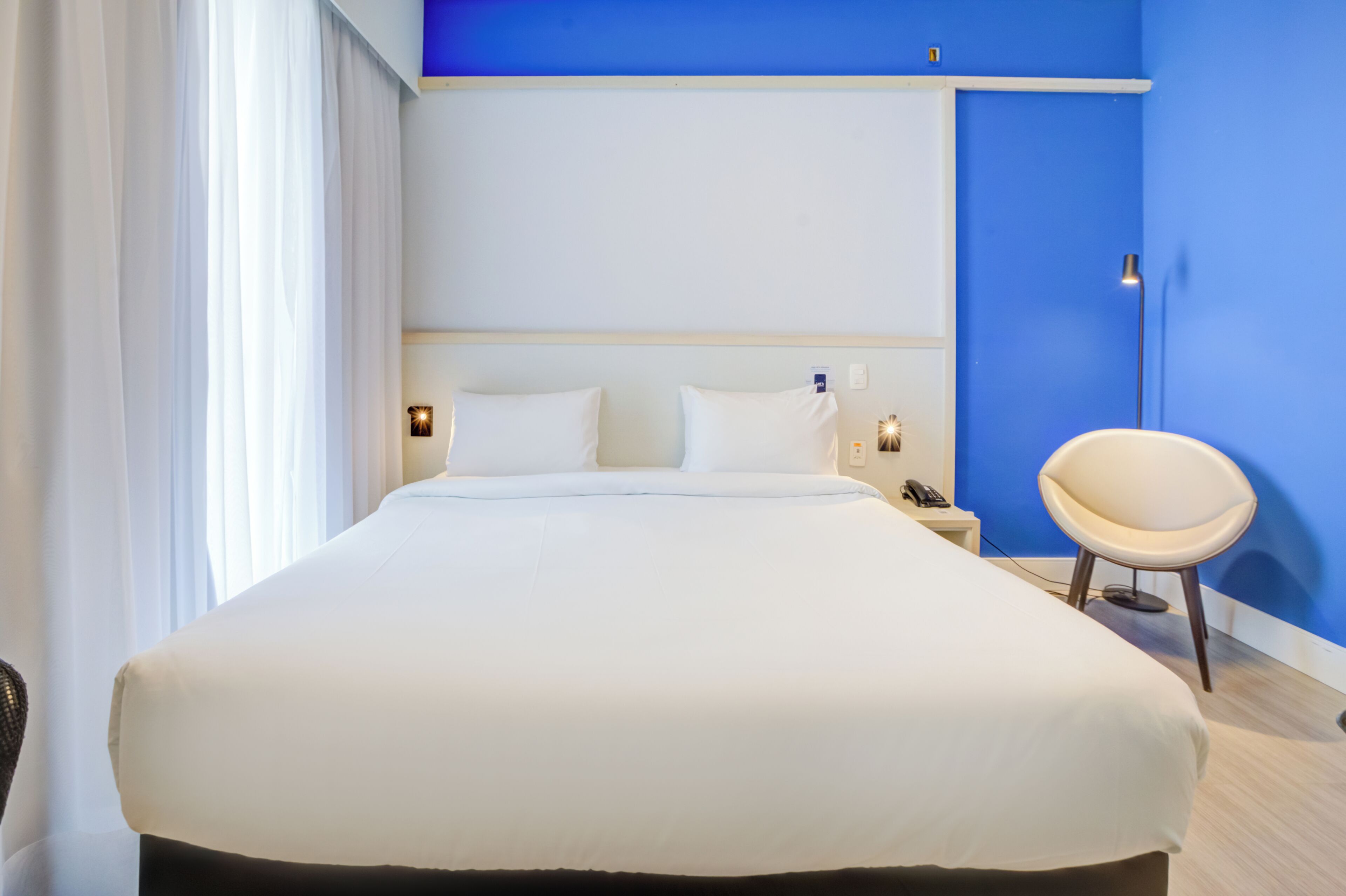 Een hotelkamer met een groot bed, nachtkastjes, een stoel en een blauwe accentmuur.