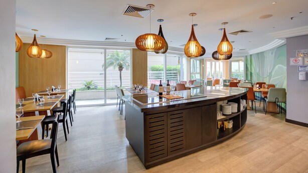 A modern dining area with a central bar, multiple tables, chairs, and pendant lighting. - Comfort Hotel Ibirapuera (São Paulo)