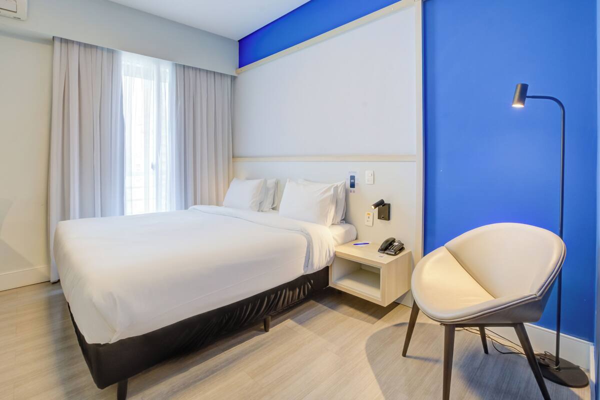 Ein Hotelzimmer mit Bett, Stuhl, Nachttisch und einer Schreibtischlampe.