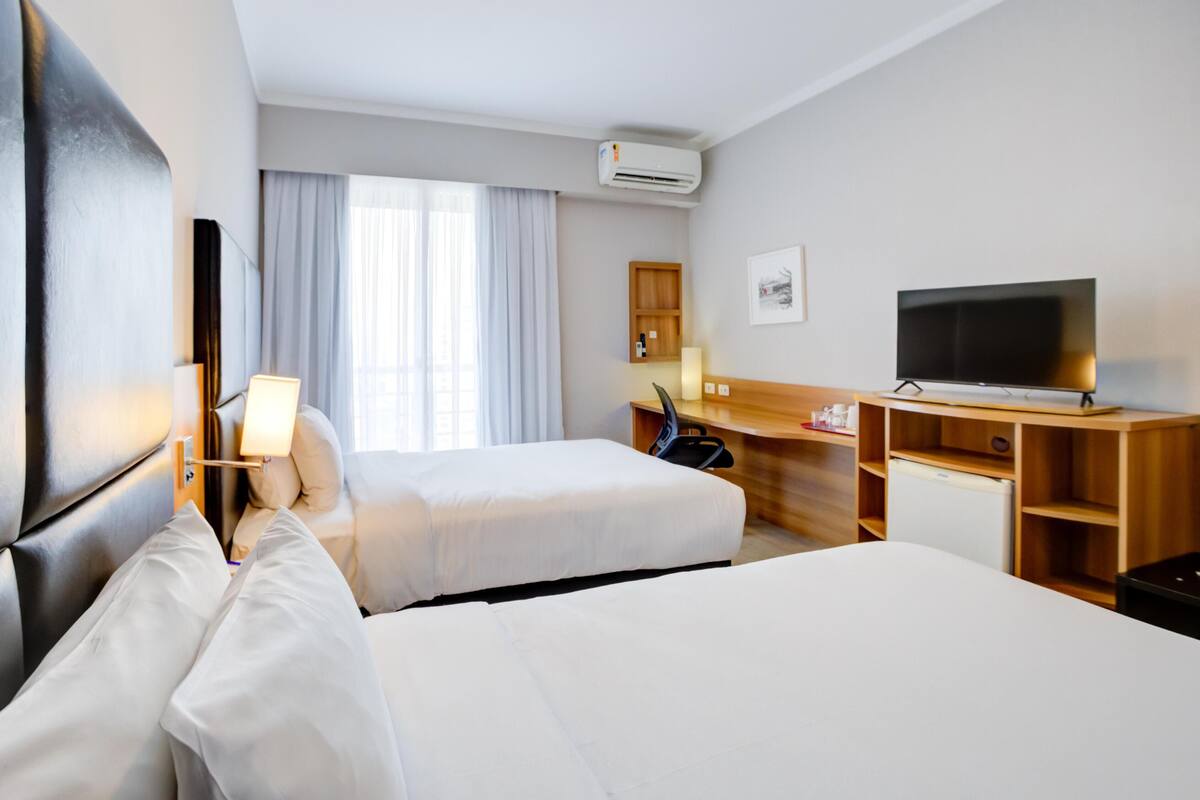 Ein Hotelzimmer mit zwei Betten, einem Schreibtisch, einem Fernseher und einer Klimaanlage.