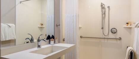 A modern bathroom with a large mirror, two sinks, a shower with a handheld showerhead, and a towel rack.