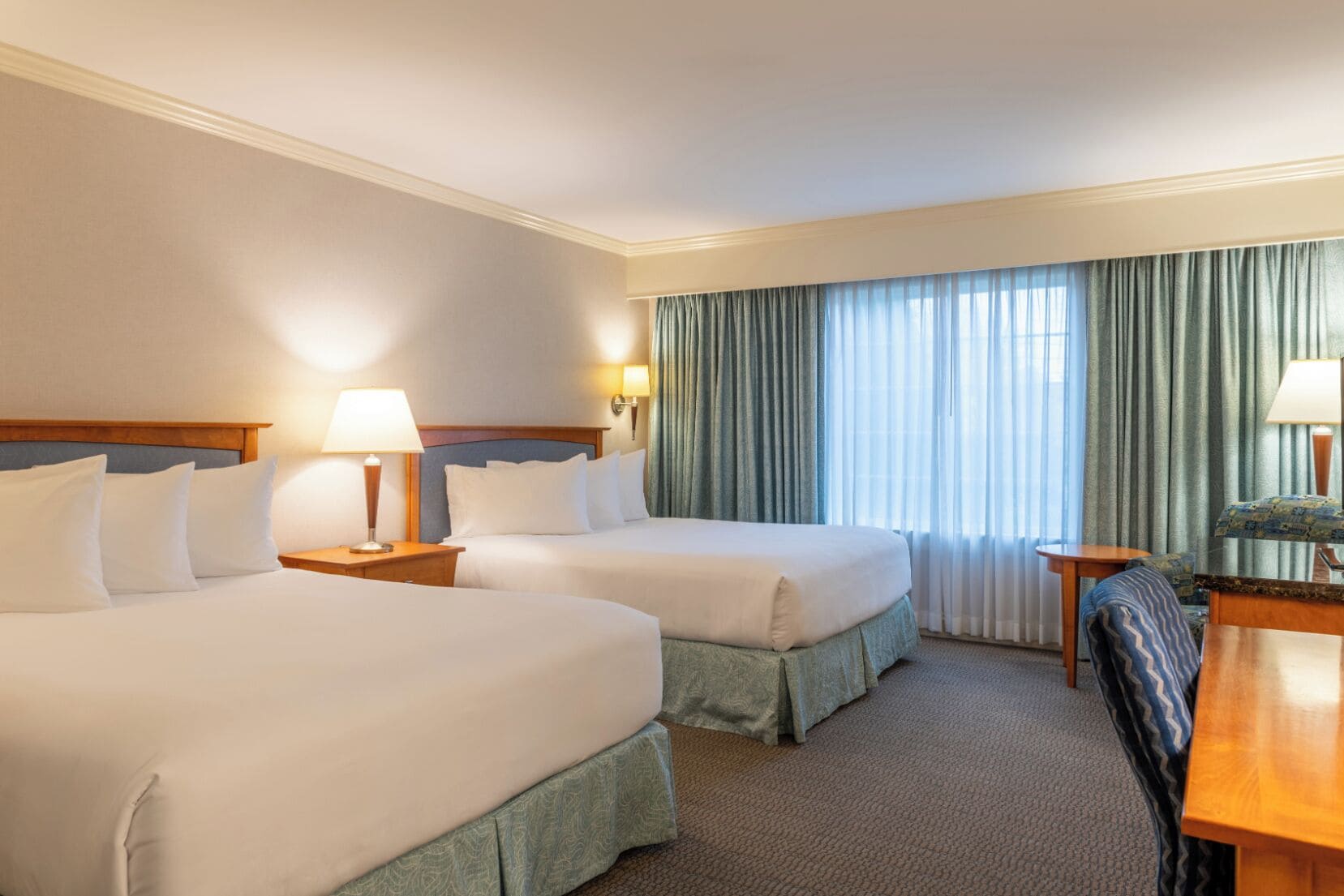 A hotel room with two beds, a desk, a chair, and a window with curtains.
