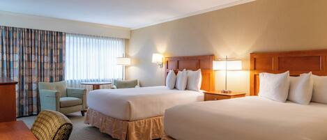 A hotel room with two beds, a desk, a chair, and a window with curtains.