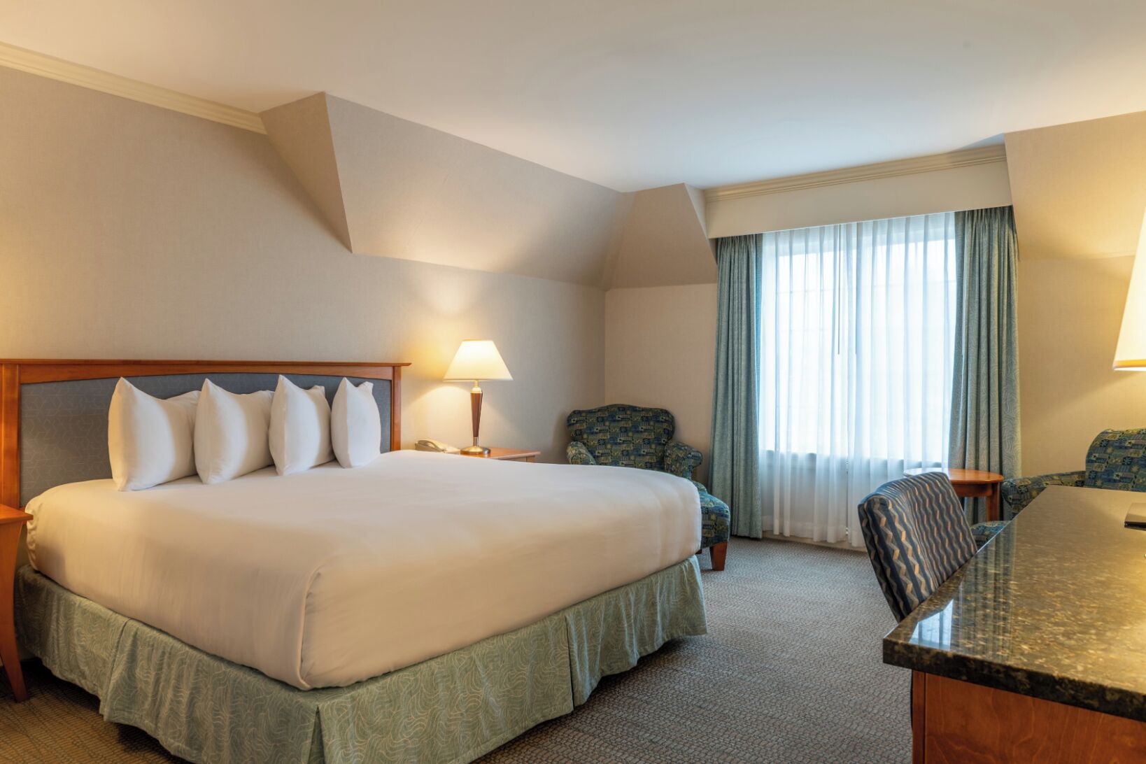 Une chambre d’hôtel avec un grand lit, deux chaises, un bureau et une fenêtre avec des rideaux.