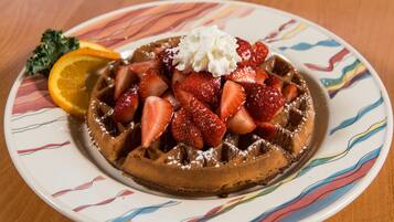 Un gaufre garni de fraises, de crème fouettée et d’une tranche d’orange, le tout présenté sur une assiette colorée.