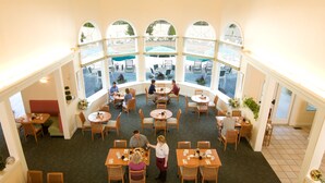 A restaurant with multiple tables and chairs, large windows overlooking a pool area.