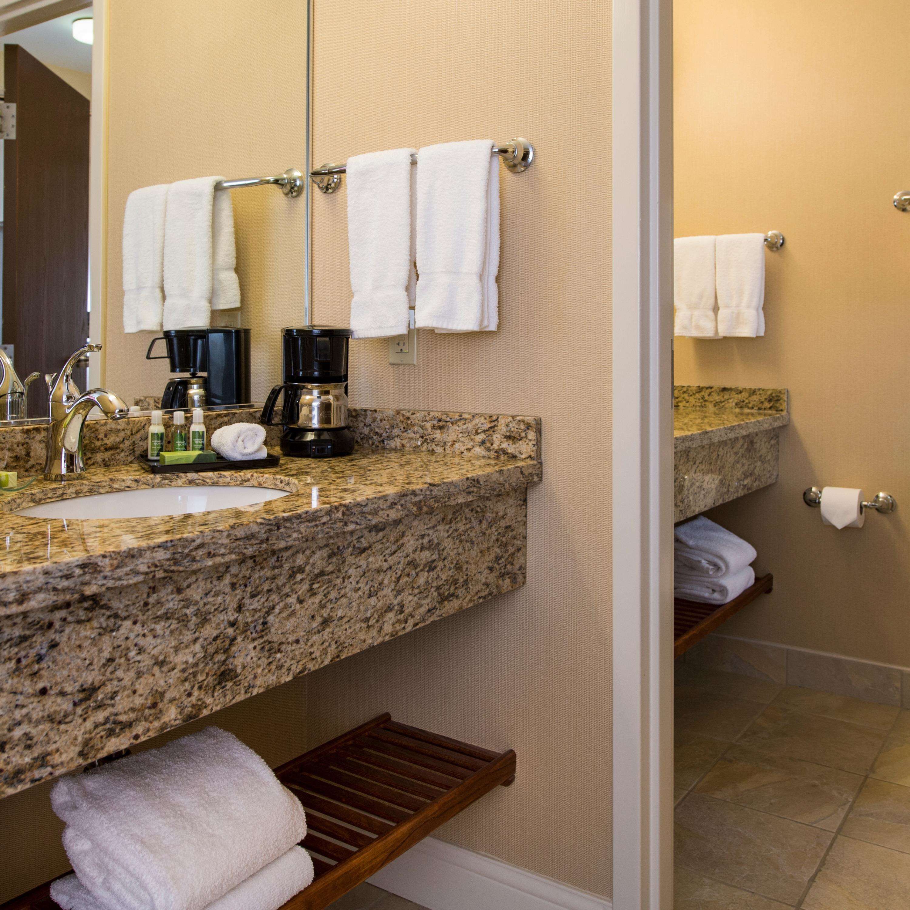 A bathroom with a granite countertop, a sink, a coffee maker, and a towel rack.