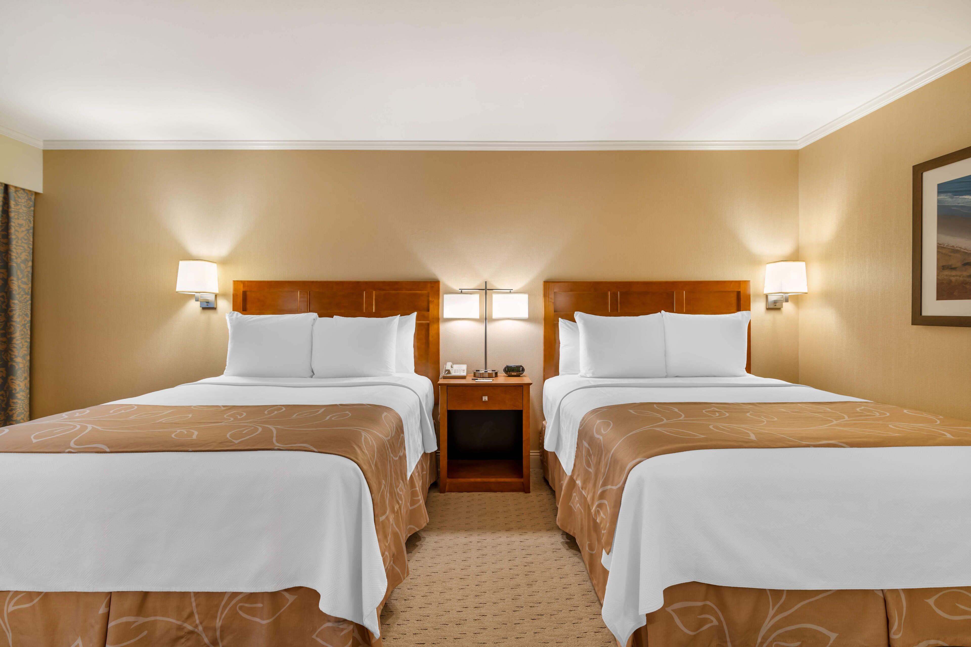 Une chambre d’hôtel avec deux lits, une table de chevet et une lampe placée entre les lits.