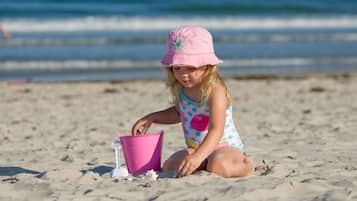 Un niño jugando con un cubo rosa en una playa arenosa.