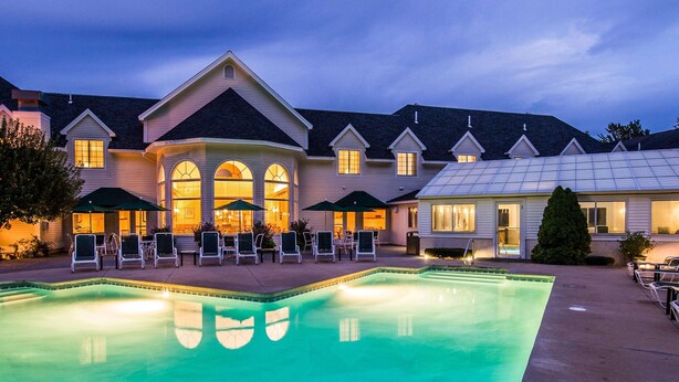 A hotel with a swimming pool, outdoor seating, and a covered patio area.