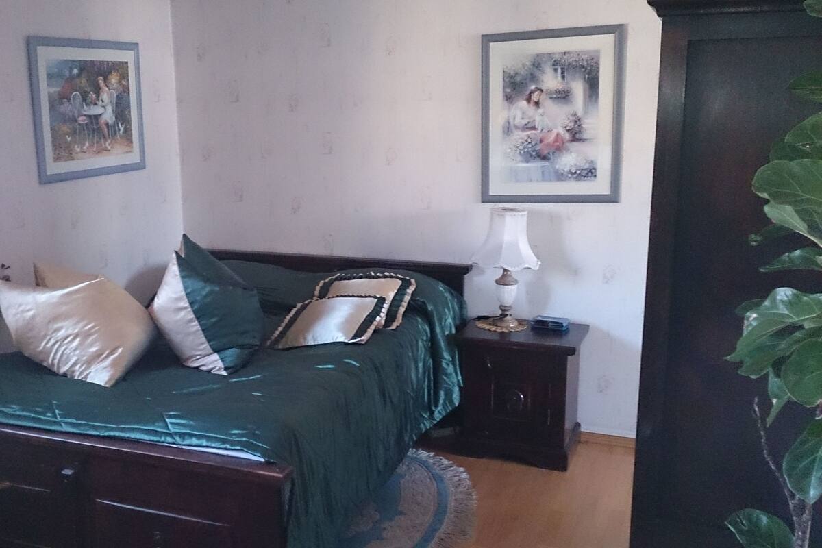 A bedroom with a bed, pillows, a bedside table with a lamp, and two framed pictures on the wall.