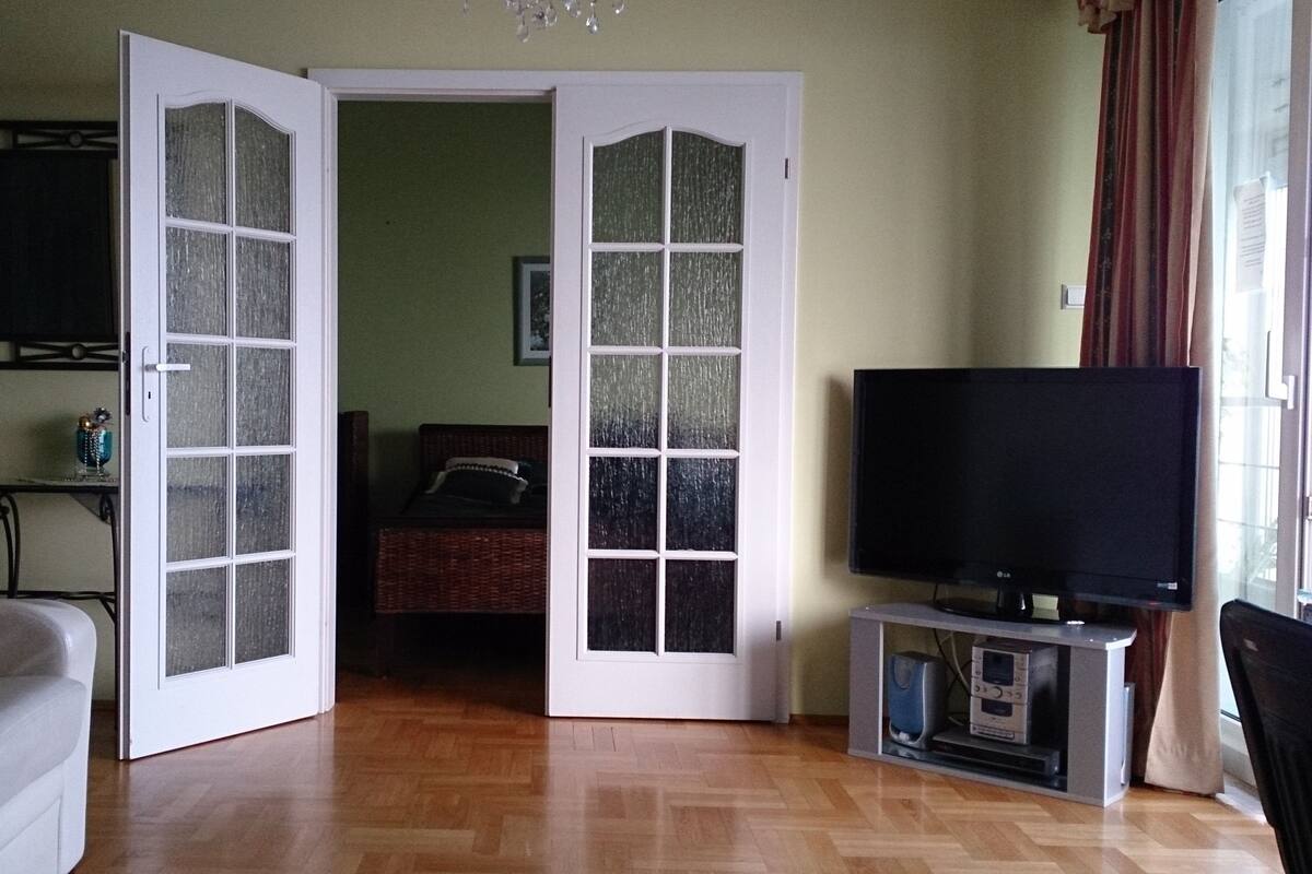 An open door leading to a bedroom with a bed, a television on a stand, and a small table with a decorative item.