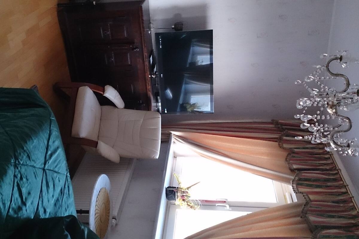 A room with a bed, a chair, a TV, and a chandelier.