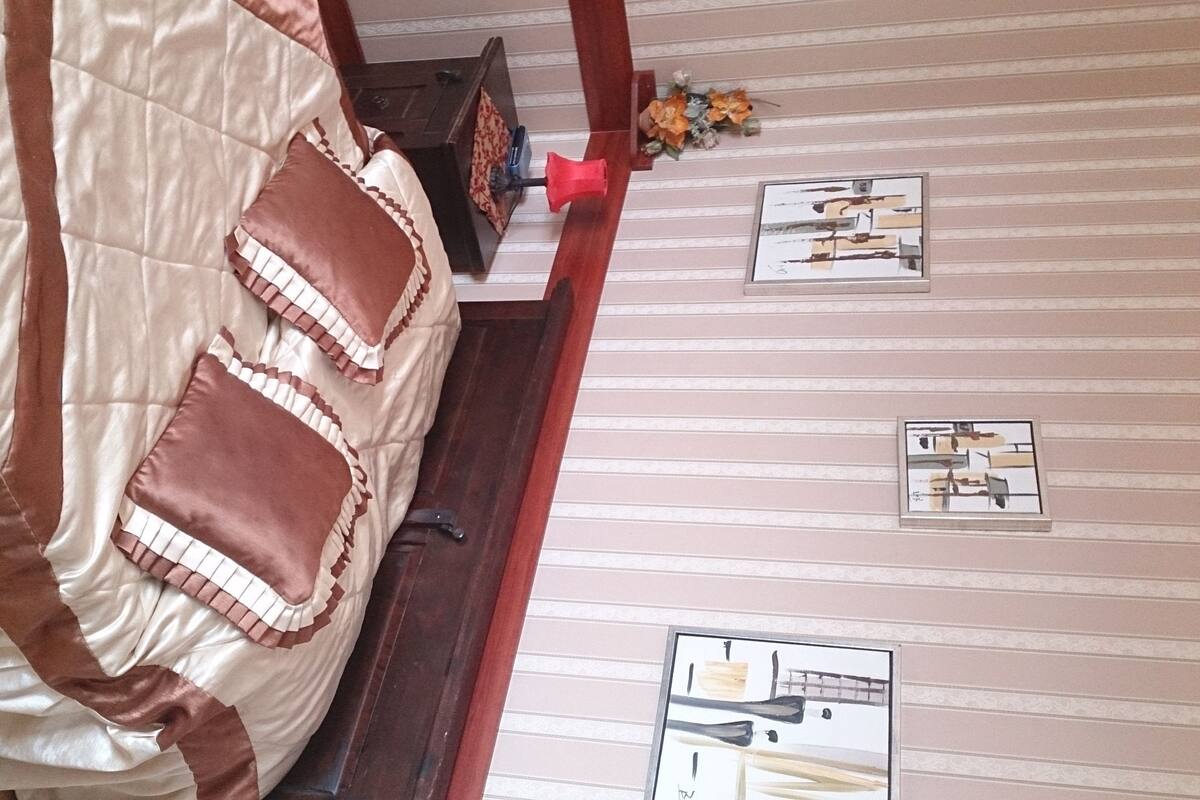A bedroom with a bed, pillows, a nightstand, and a wall with framed pictures.