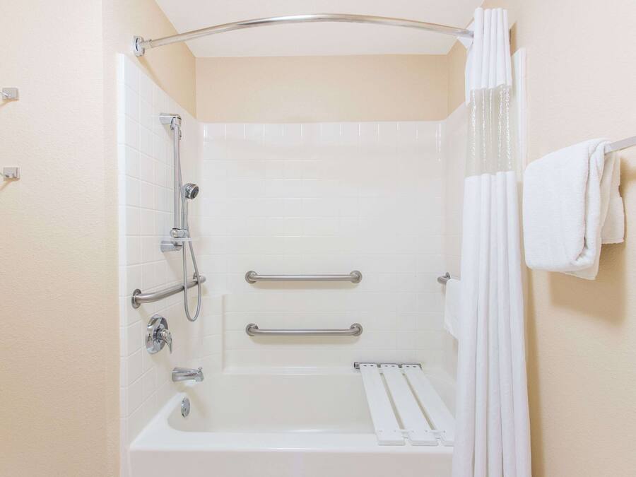 A bathroom with a bathtub, grab bars, a shower curtain, and a towel rack.